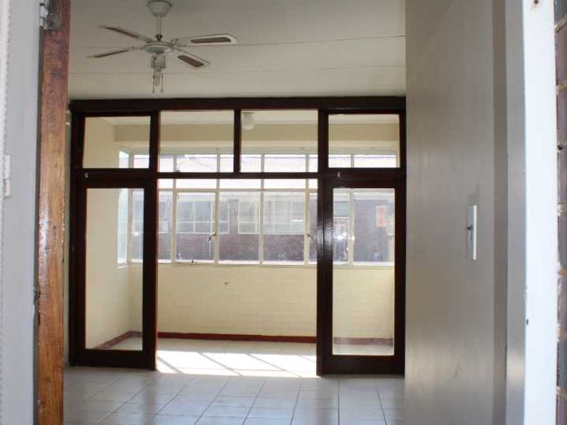 An empty living area featuring tiled floors, a ceiling fan, and large timber-framed glass doors leading to an enclosed balcony space.