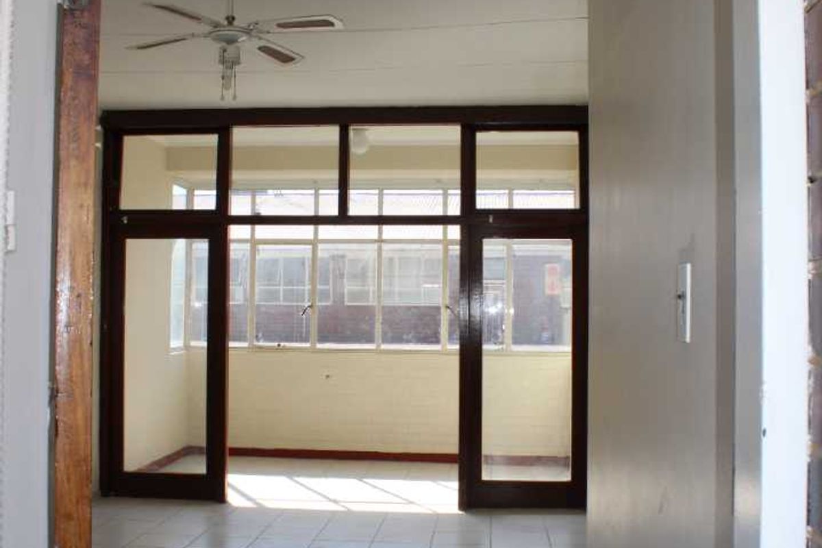 An empty living area featuring tiled floors, a ceiling fan, and large timber-framed glass doors leading to an enclosed balcony space.