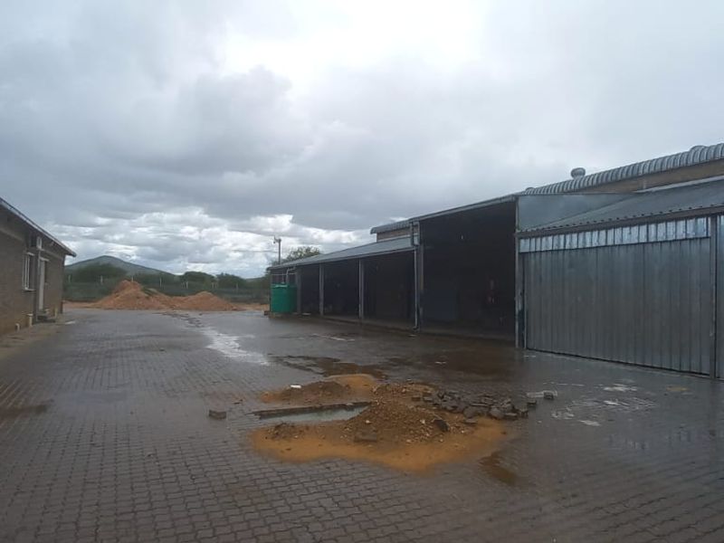 Industrial yard area featuring paved surfaces, brick buildings, and open-bay storage structures under a cloudy sky.