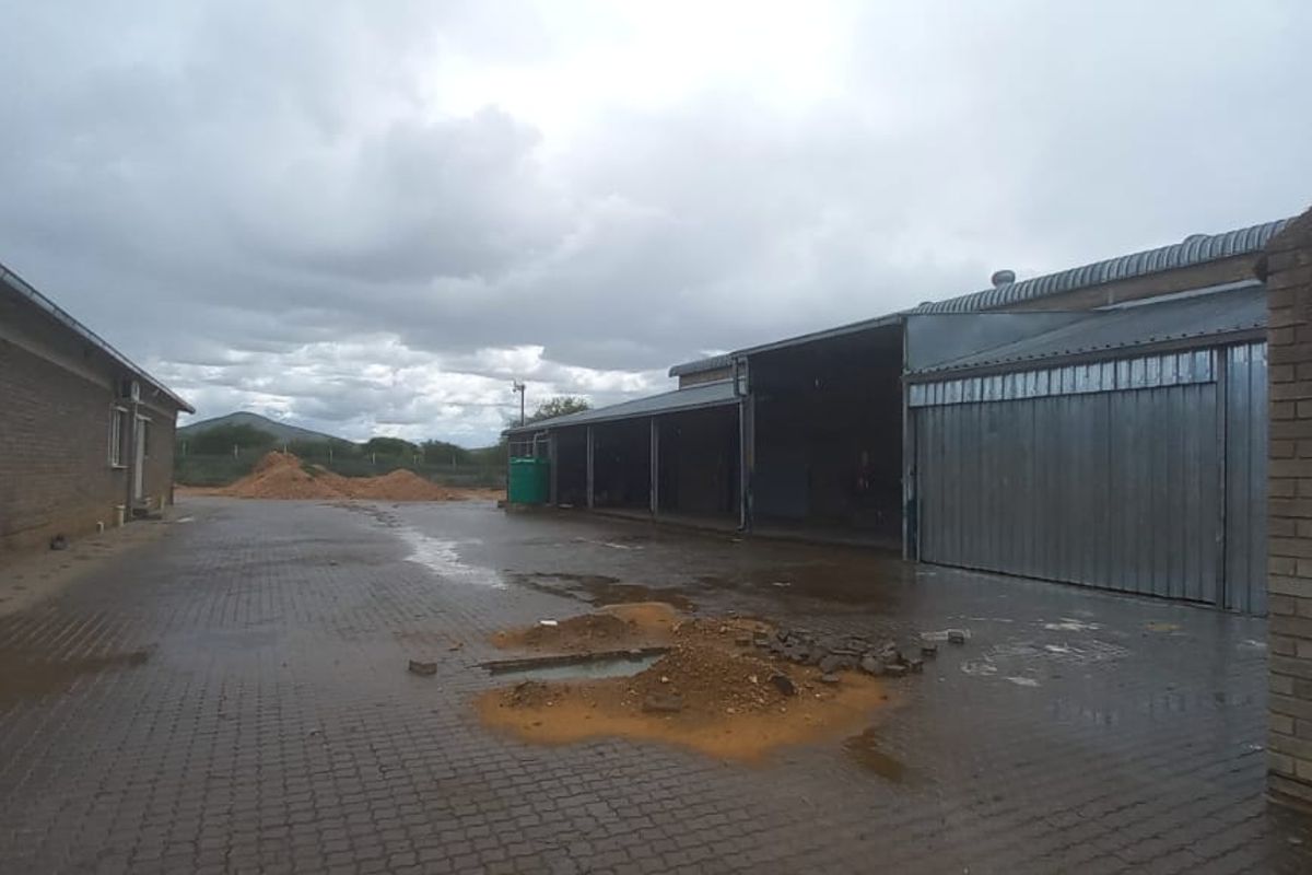 Industrial yard area featuring paved surfaces, brick buildings, and open-bay storage structures under a cloudy sky.