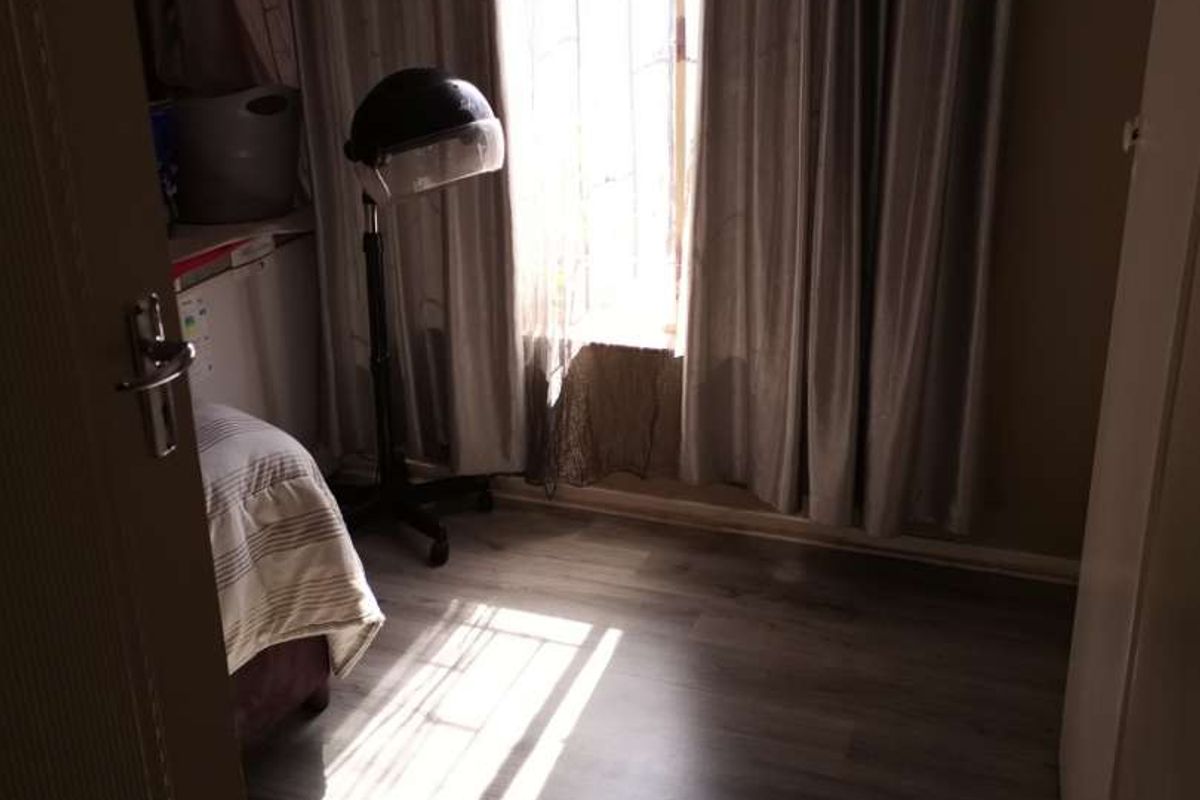 A bedroom featuring laminate flooring and natural light entering through a window with curtains.
