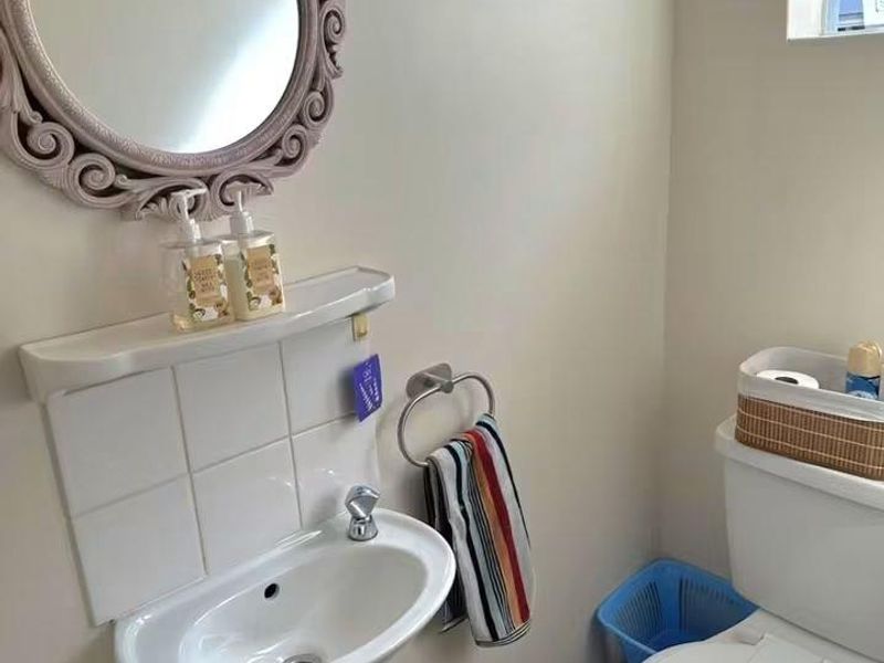 A compact bathroom featuring a wall-mounted basin with tiled splashback, a standard toilet, and a window for natural light.