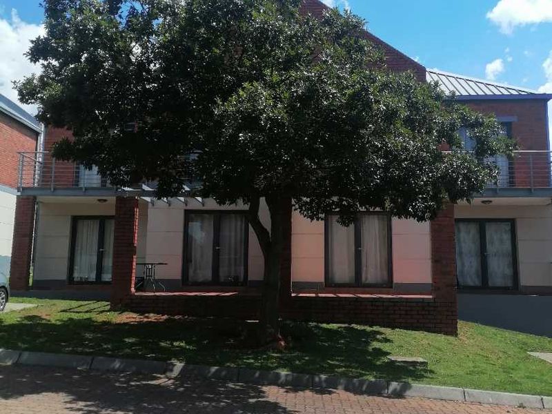Front view of a brick apartment building featuring a paved driveway, mature tree, and balconies with metal railings.