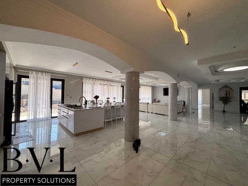 Spacious open-plan living area featuring a modern kitchen island, polished tiled flooring, and elegant arched columns, creating a bright and airy atmosphere.