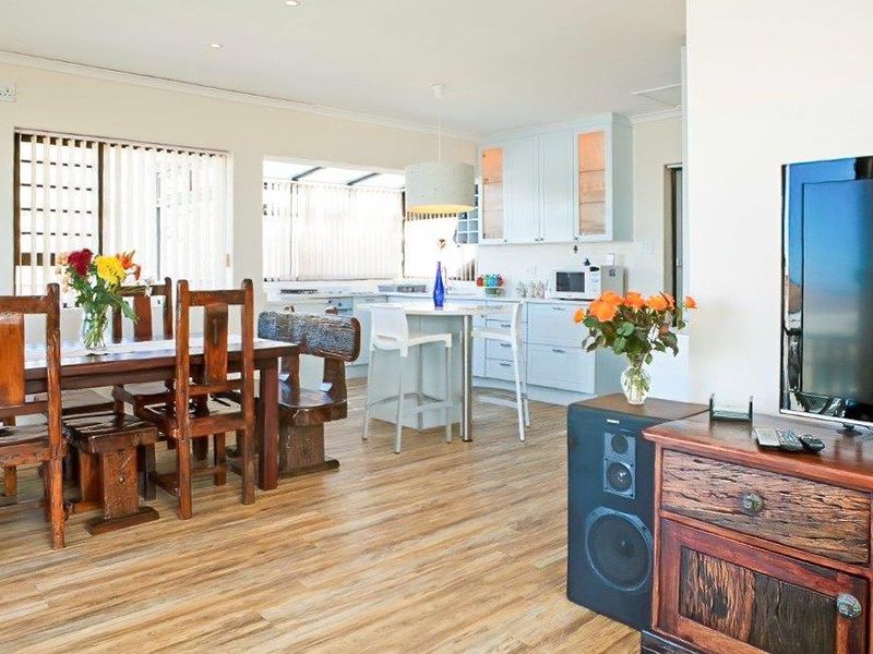 Spacious open-plan living and dining area featuring light-toned laminate flooring, a functional kitchen with island, and direct access to outdoor space via sliding doors.