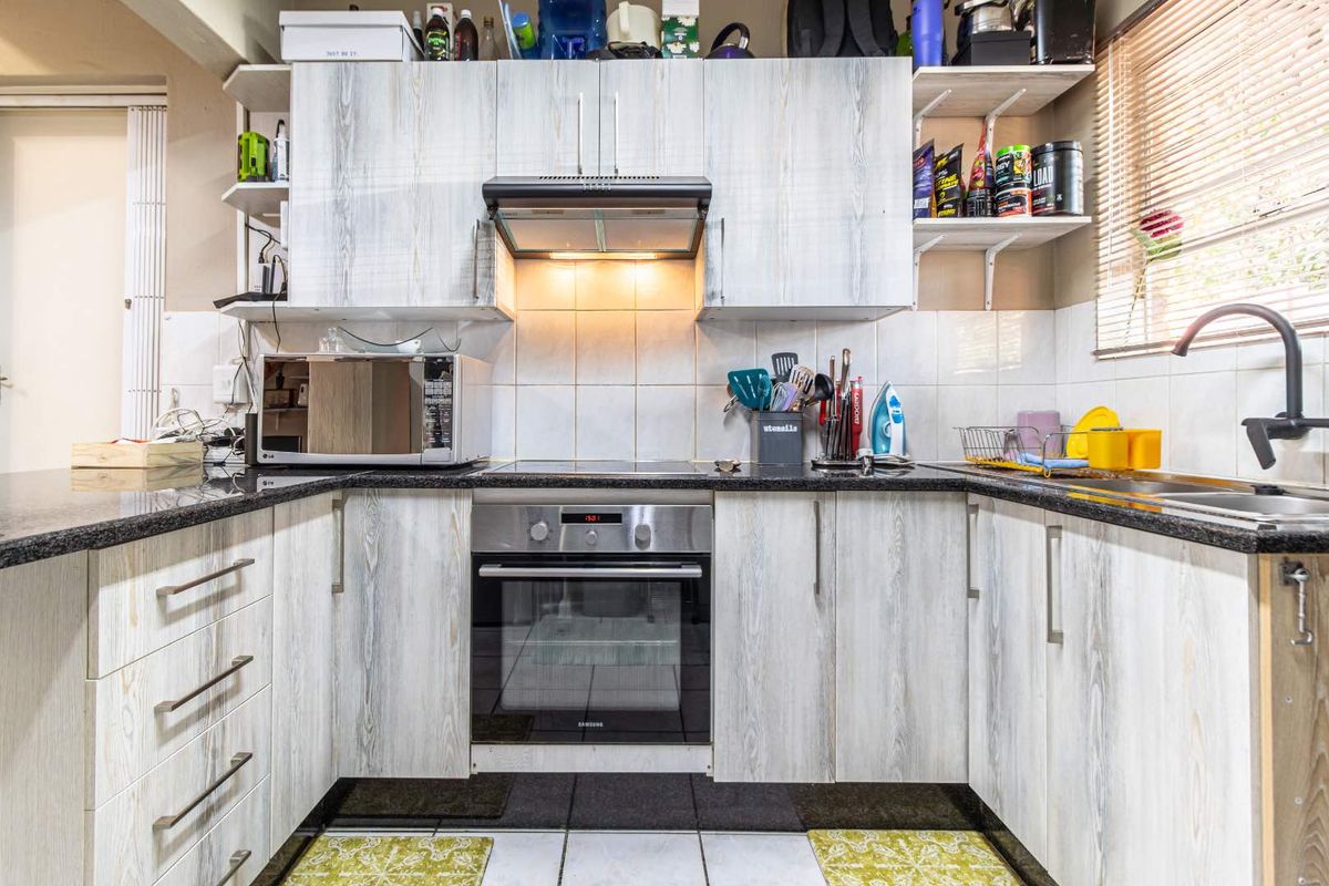 A functional U-shaped kitchen featuring light wood-grain cabinetry, granite countertops, a built-in oven with hob, and a tiled backsplash.