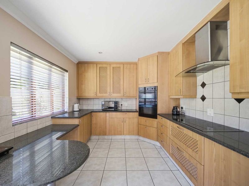 A functional kitchen featuring light wood cabinetry, dark granite countertops, a tiled backsplash, and integrated appliances including an oven and extractor fan.