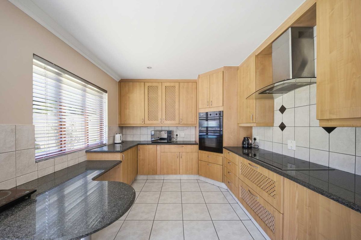 A functional kitchen featuring light wood cabinetry, dark granite countertops, a tiled backsplash, and integrated appliances including an oven and extractor fan.