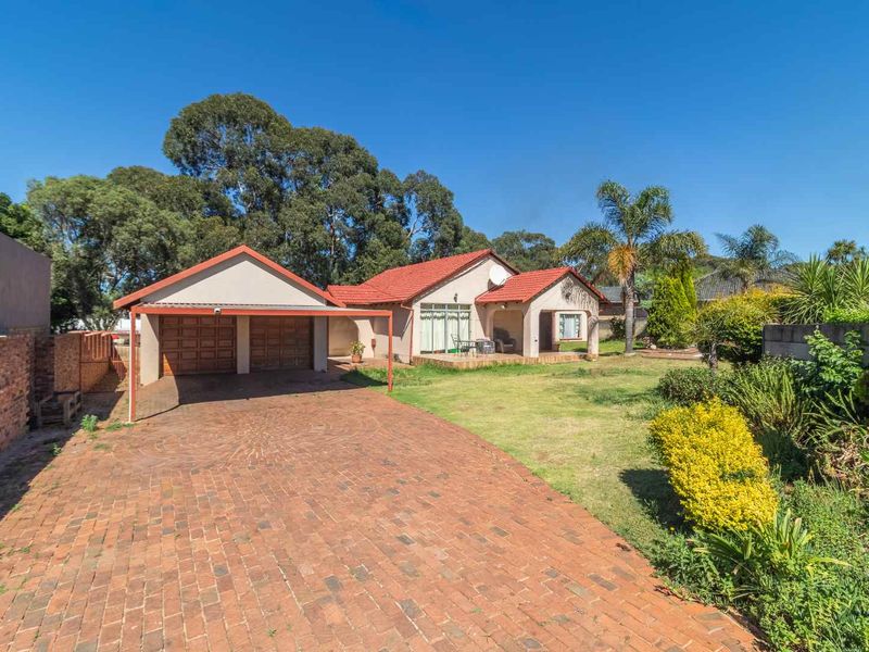 A well-maintained single-story house featuring a double garage, brick-paved driveway, and a covered patio set within a landscaped garden.
