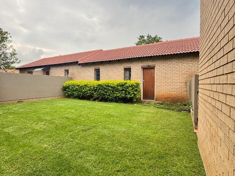 A private rear garden area featuring a well-maintained lawn, brick boundary walls, and a classic brick townhouse facade with a tiled roof.