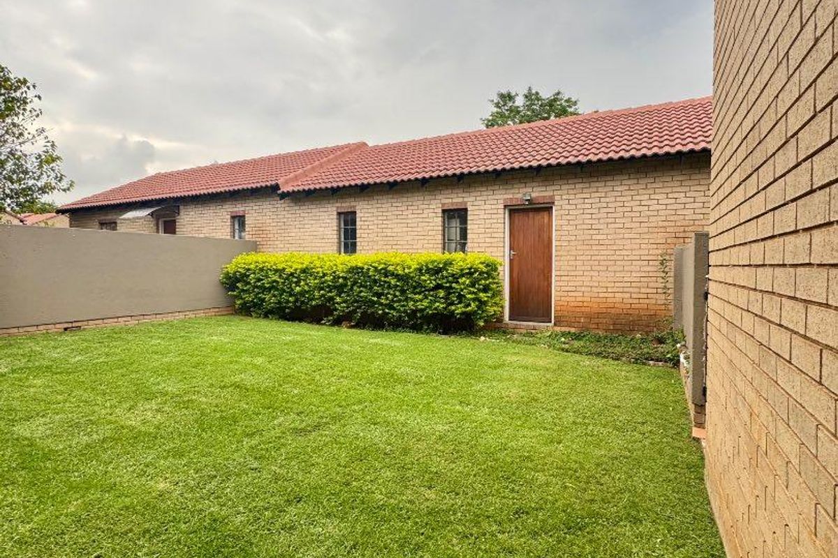 A private rear garden area featuring a well-maintained lawn, brick boundary walls, and a classic brick townhouse facade with a tiled roof.