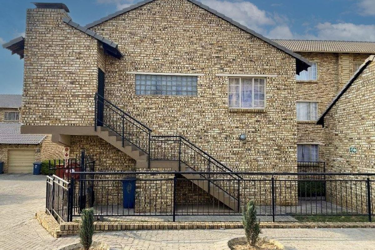 Exterior view of a multi-story apartment building featuring face brick construction, an external staircase with metal railings, and paved ground level access.