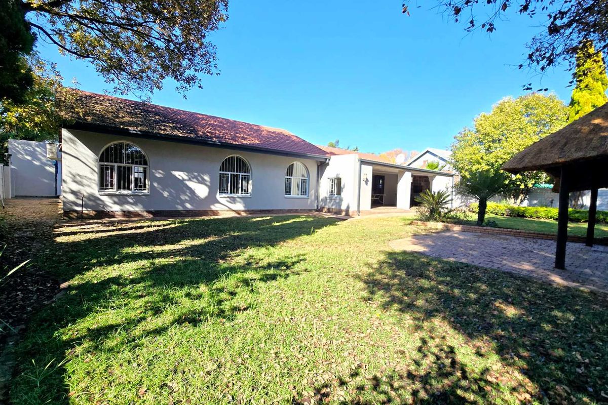 Rear view of the house featuring a spacious lawn, a brick-paved patio area, and a traditional thatched lapa, perfect for outdoor entertaining.