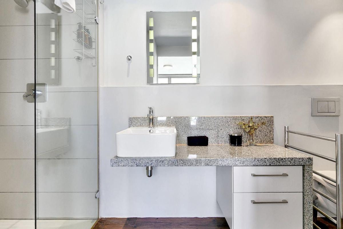 Modern bathroom featuring a glass-enclosed shower, granite vanity with vessel sink, lighted mirror, and a heated towel rail.