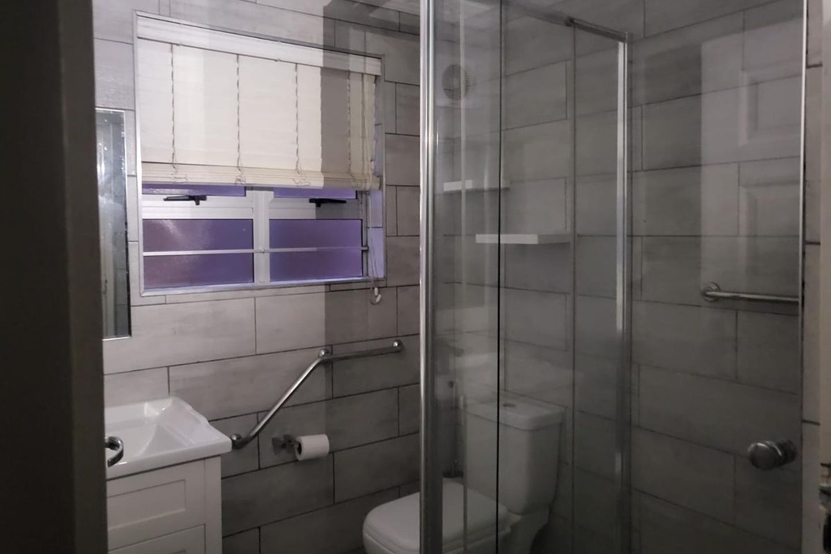 A modern bathroom featuring a glass shower enclosure, vanity basin, toilet, and tiled walls with an installed grab rail for accessibility.