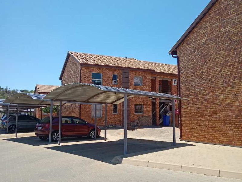 Exterior view of a face brick apartment complex featuring covered parking bays and paved driveway access.