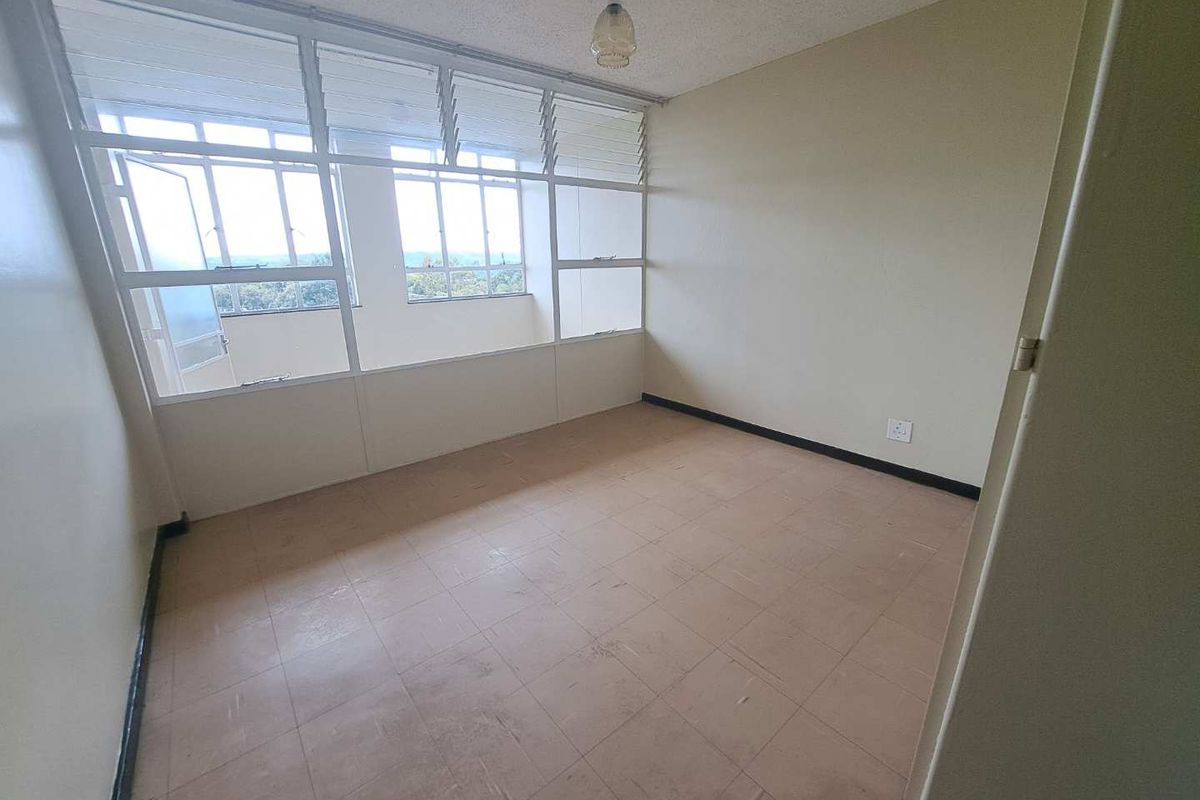 An empty bedroom featuring large windows with louvre panes, tiled flooring, and neutral wall finishes, offering a blank canvas for renovation.