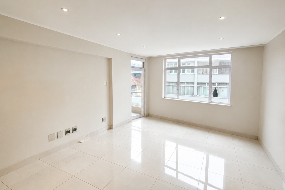 A bright, empty living room featuring neutral walls, polished porcelain floor tiles, recessed downlights, and large aluminium-framed windows providing natural light.