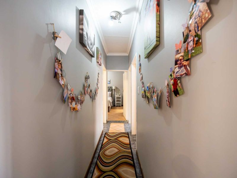 A well-lit interior hallway featuring tiled flooring, neutral wall finishes, and a central ceiling light fixture, providing access to adjacent rooms.