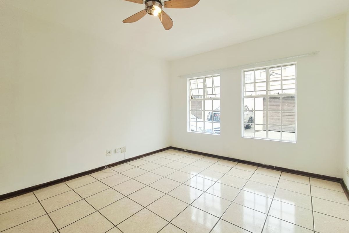 A bright, empty bedroom featuring neutral tiled flooring, a ceiling fan, and large grid-pattern windows allowing for natural light.