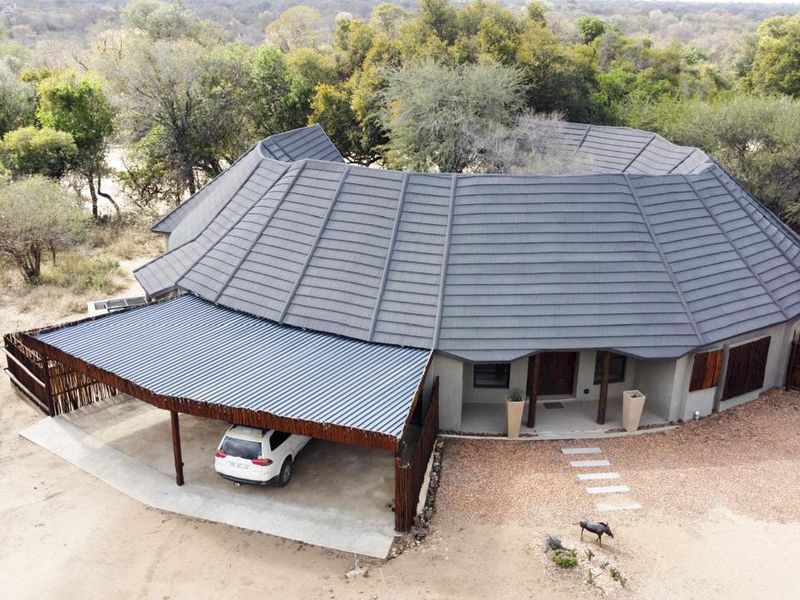 Aerial view of a modern house featuring a large tiled roof, a covered carport, and a natural bushveld setting.