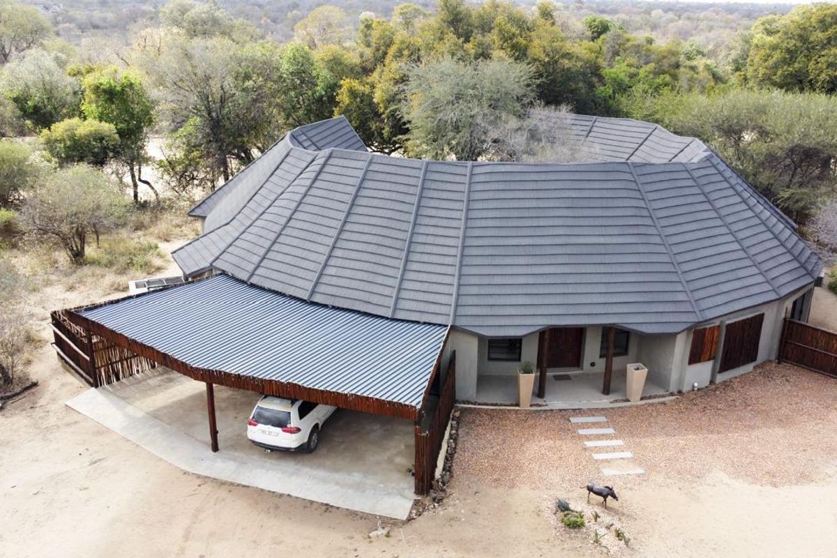 Aerial view of a modern house featuring a large tiled roof, a covered carport, and a natural bushveld setting.