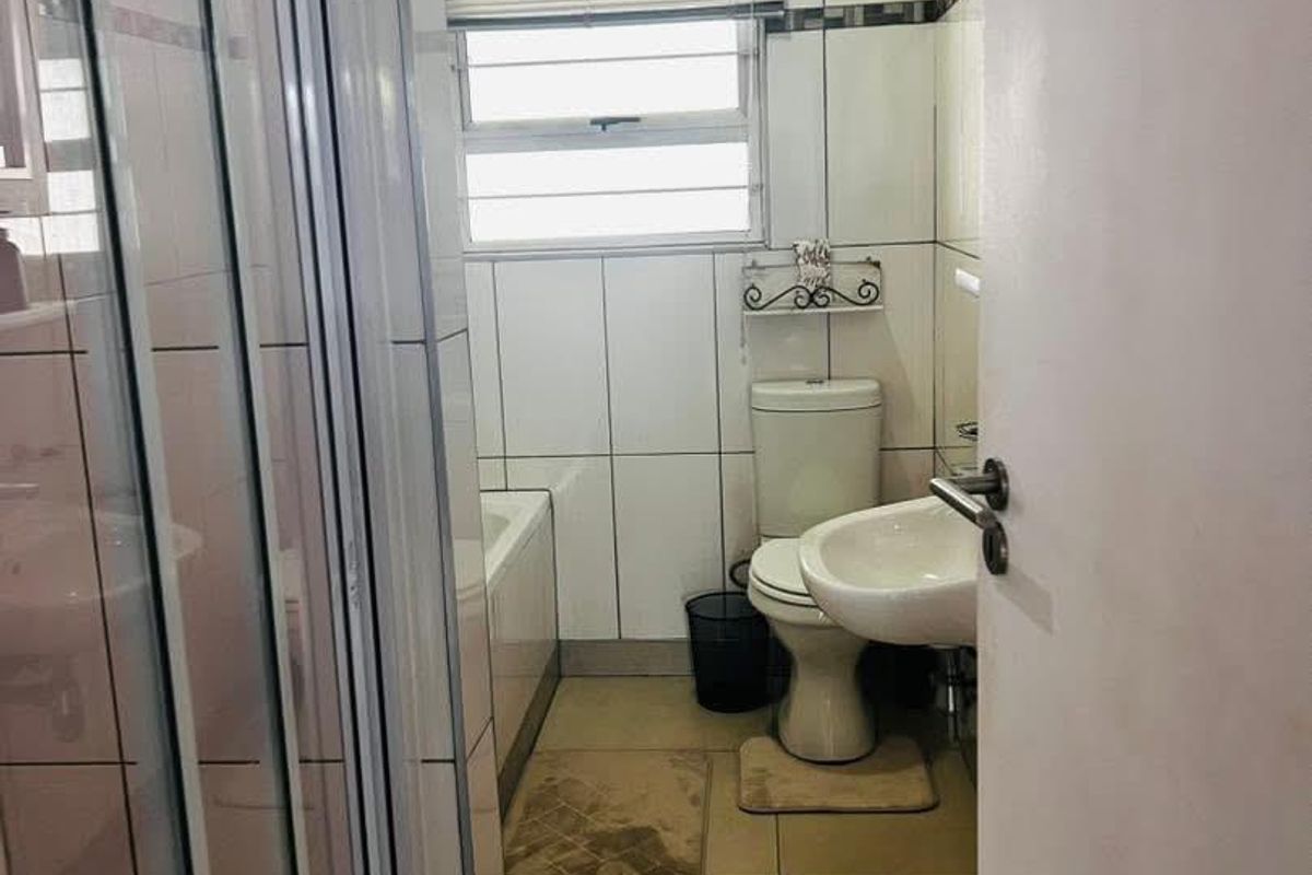 A functional bathroom featuring a shower enclosure, bathtub, toilet, and wall-mounted basin with tiled walls and flooring.