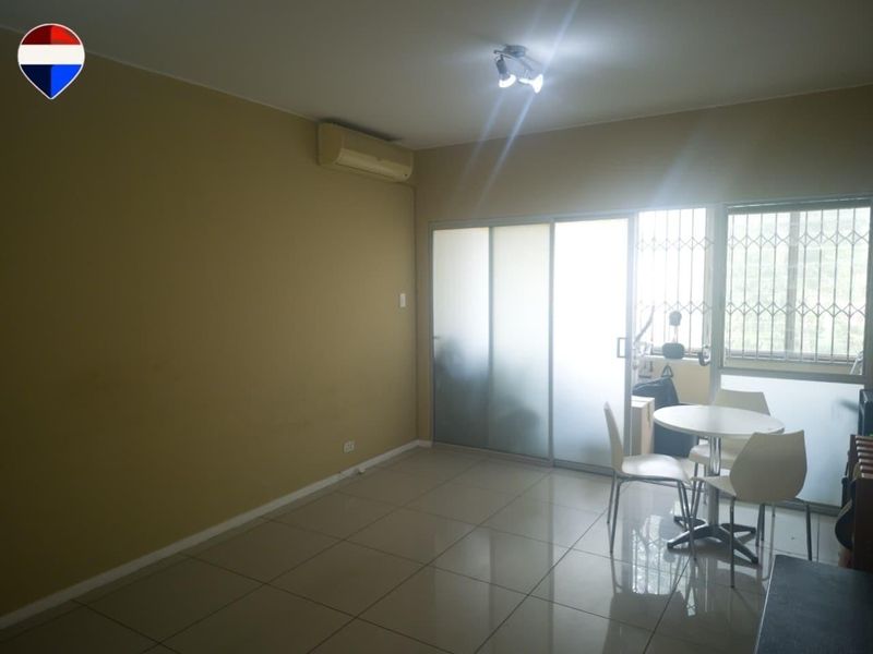 A living area featuring tiled flooring, a wall-mounted air conditioning unit, and sliding glass doors leading to an outdoor space with security gates.