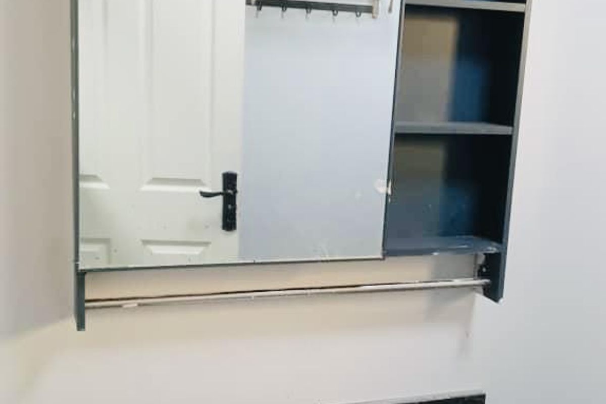 A bathroom vanity area featuring a dark stone countertop, integrated sink, and a wall-mounted mirrored cabinet with open shelving.