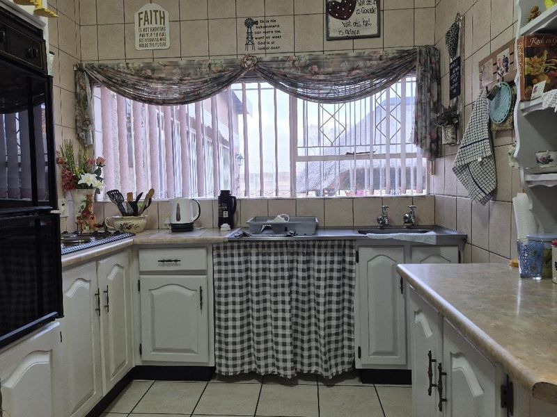 A functional kitchen featuring tiled splashbacks, laminate countertops, a built-in oven, and a double sink with security bars on the window.