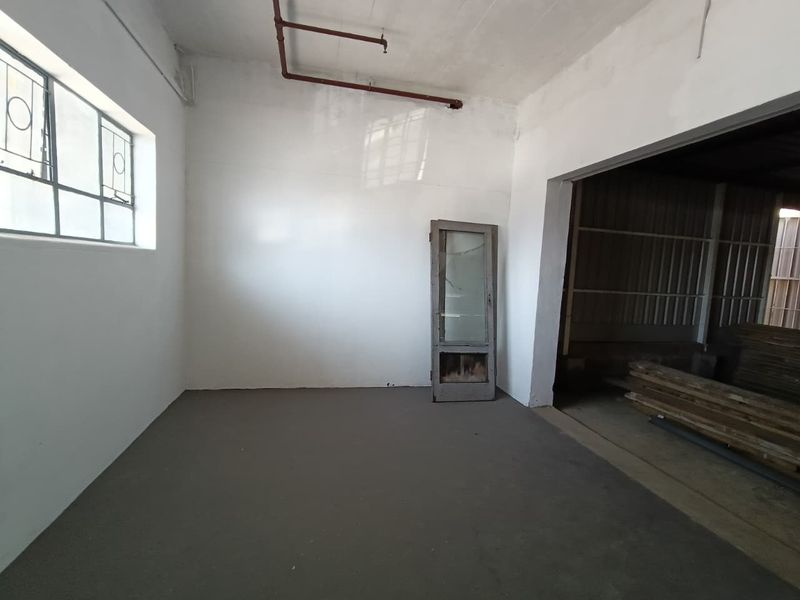 An empty industrial utility space featuring exposed fire sprinkler piping, concrete flooring, and steel-framed windows.