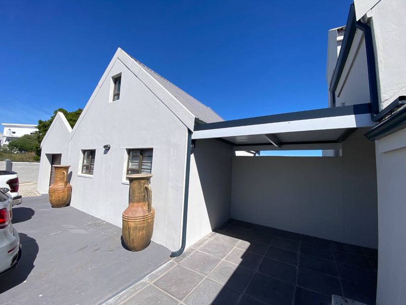 A well-maintained exterior view of the property featuring a paved driveway, a covered carport, and clean white facade finishes.