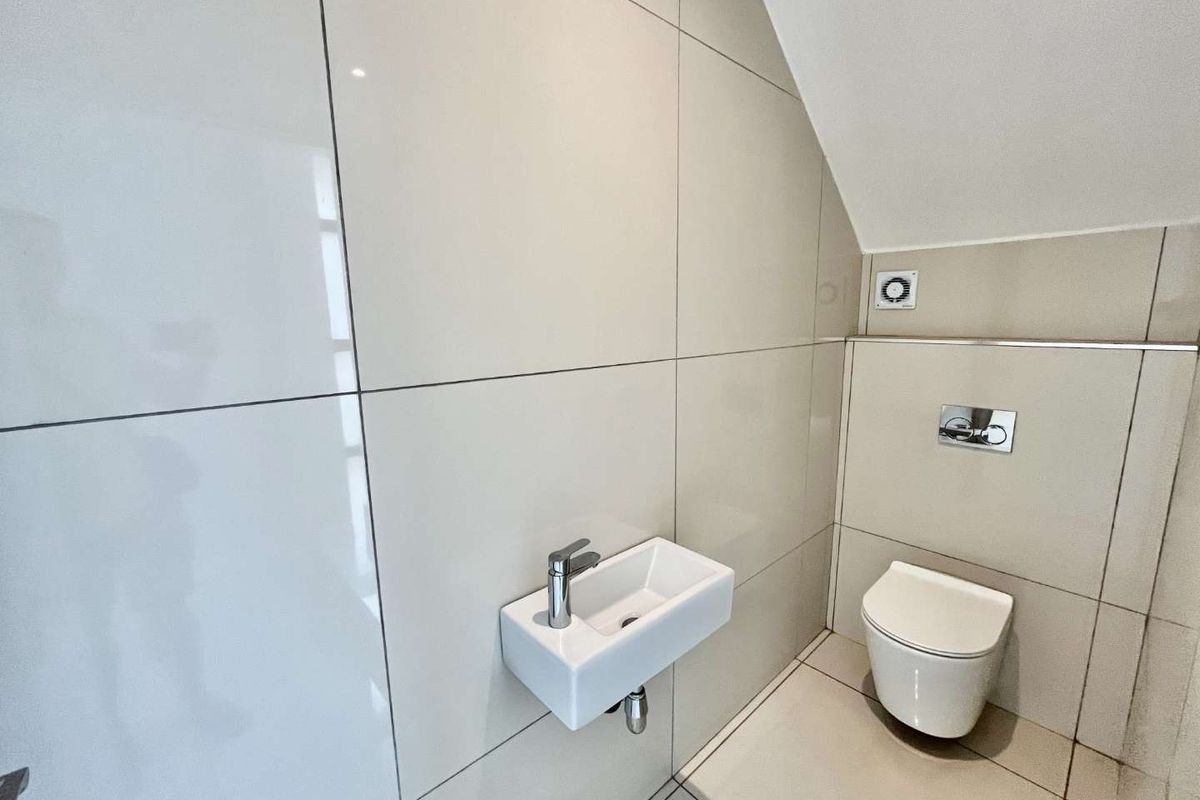 A modern guest cloakroom featuring large-format wall tiles, a wall-mounted toilet with a concealed cistern, and a compact wall-hung basin.