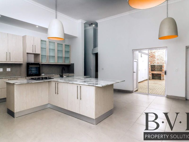 Spacious open-plan kitchen featuring light wood cabinetry, stone countertops, and integrated appliances, flowing seamlessly to an outdoor patio area.