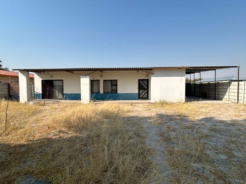 Rear view of the property featuring a covered patio area, concrete boundary walls, and a large unmaintained yard space.