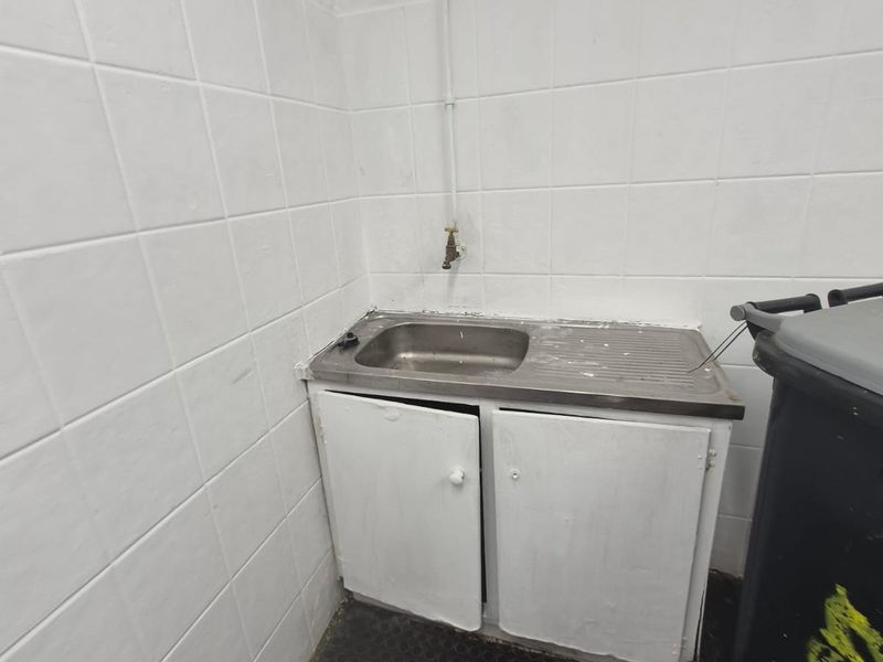 A basic utility area featuring a stainless steel sink, tiled walls, and built-in cabinetry, suitable for laundry or storage purposes.