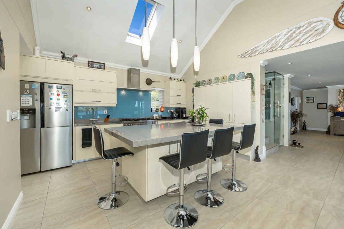Modern kitchen featuring a central island with breakfast bar seating, sleek cabinetry, a blue glass splashback, and a vaulted ceiling with a skylight.