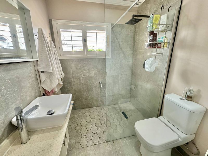 Modern bathroom featuring a vessel sink on a stone vanity, a walk-in shower with a rain shower head, and stylish hexagonal floor tiling.