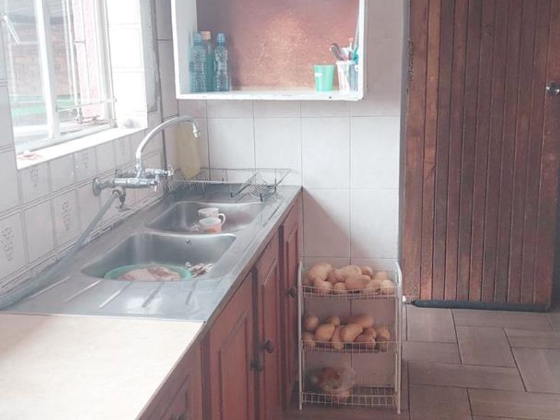 A functional kitchen featuring wooden cabinetry, a double basin stainless steel sink, tiled splashbacks, and durable tiled flooring.