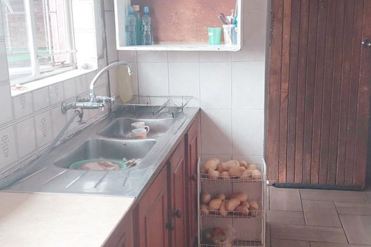 A functional kitchen featuring wooden cabinetry, a double basin stainless steel sink, tiled splashbacks, and durable tiled flooring.