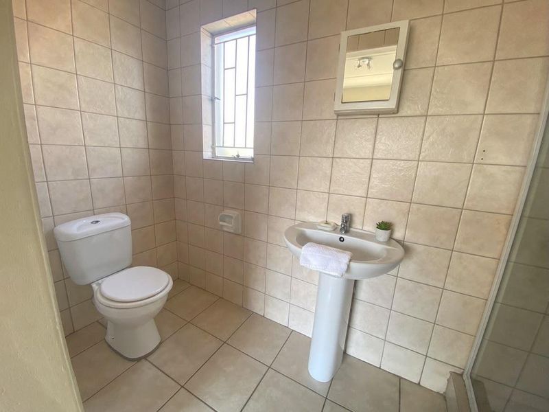 A functional bathroom featuring a pedestal basin, toilet, and neutral wall and floor tiling with a window for natural light.