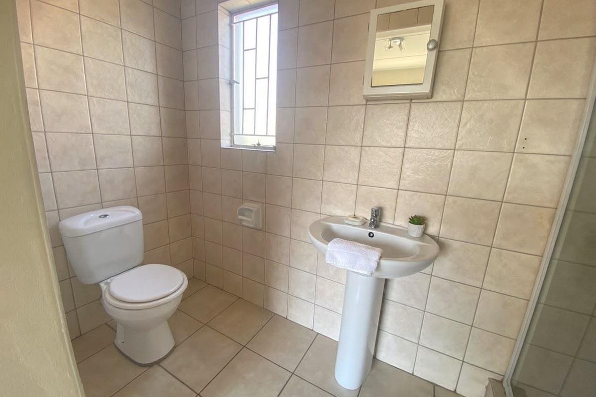 A functional bathroom featuring a pedestal basin, toilet, and neutral wall and floor tiling with a window for natural light.