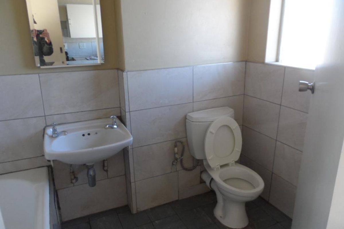 A functional bathroom featuring a standard toilet, wall-mounted basin, and tiled finishes, requiring some cosmetic updates to improve its overall presentation.