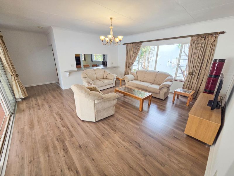 Spacious living room featuring wood-look laminate flooring, a serving hatch to the kitchen, and large windows providing natural light.