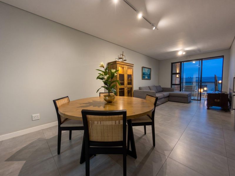 Spacious open-plan living and dining area featuring modern tiled flooring, track lighting, and large sliding glass doors leading to a balcony.