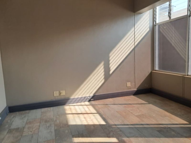 A bright, empty office space featuring tiled flooring, neutral walls, and a large window allowing for natural light.
