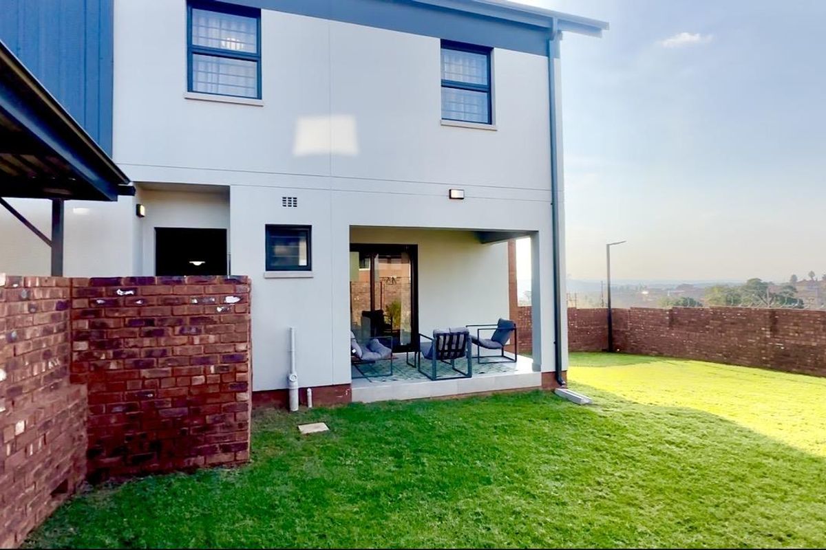 Rear view of the townhouse featuring a covered patio area, private garden, and brick boundary wall.