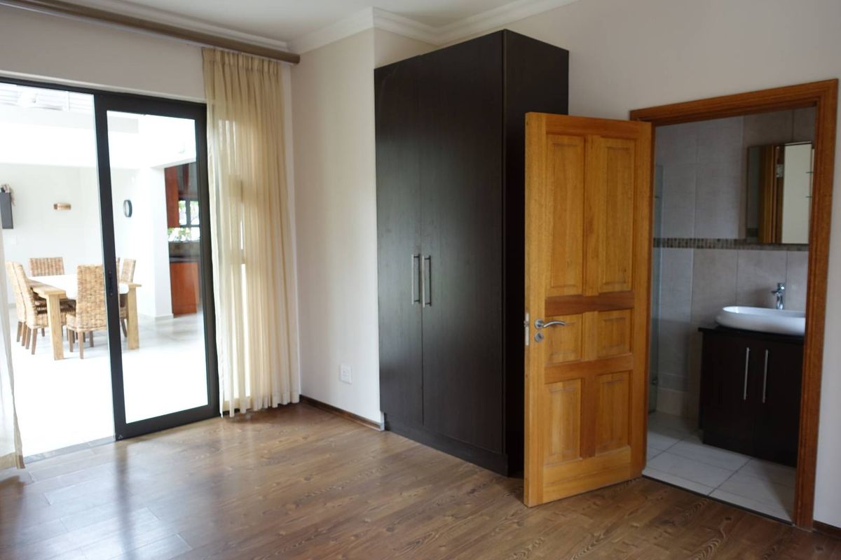 Bedroom featuring laminate flooring, a built-in dark wood wardrobe, and an en-suite bathroom with a modern vanity.