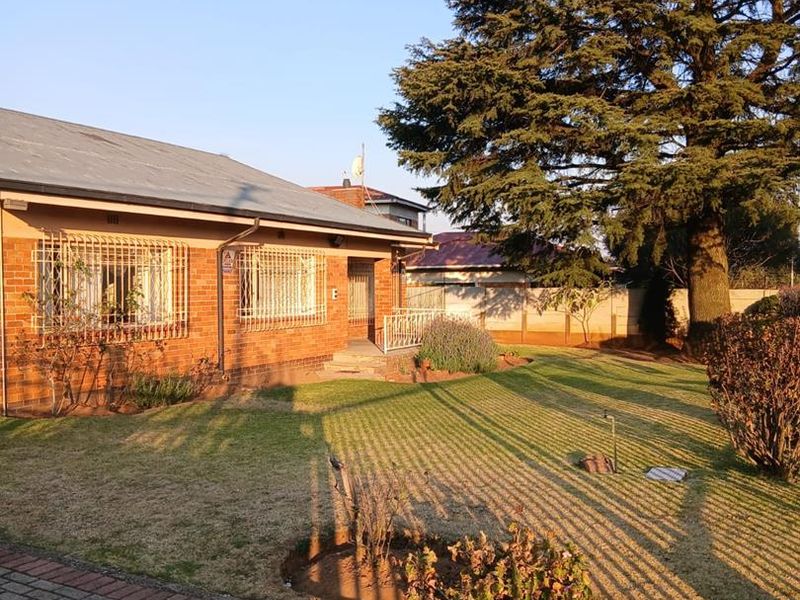 Front view of a brick house featuring a paved driveway, well-maintained lawn, and mature trees, with security bars installed on the windows.