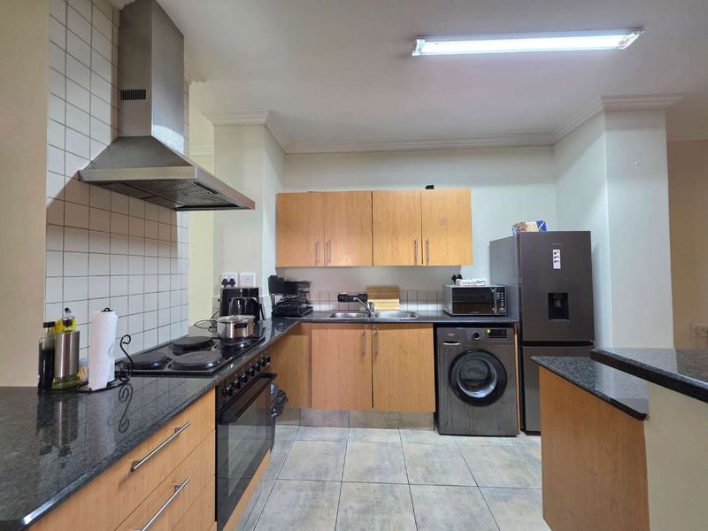 A functional kitchen featuring granite countertops, built-in cabinetry, a stainless steel extractor fan, and tiled flooring with a practical layout.